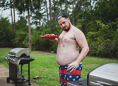 Dad, who has a 'Dad Bod,' is standing shirtless next to a barbeque grill with a plate of food in his hand;