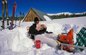 Dude chilaxing and reading a book while sitting in the snow;
